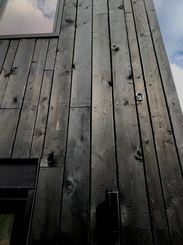 Peau de crocodile sur toutes les façades d'une maison contemporaine, entre pierre et verre. Posé il y a cinq ans — le relief accroche toujours la lumière.