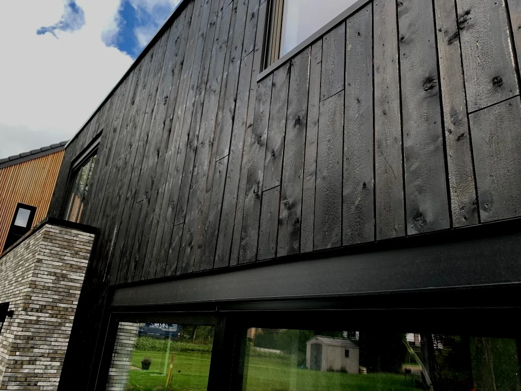Peau de crocodile sur toutes les façades d'une maison contemporaine, entre pierre et verre. Posé il y a cinq ans — le relief accroche toujours la lumière.