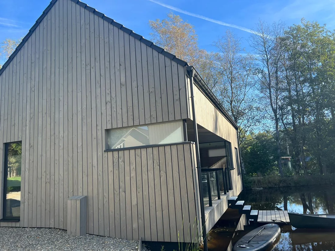 Chalets bardés en pin thermo-traité pré-grisé, pose verticale, au bord de l'eau